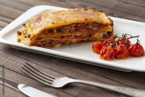 Tasty lasagna with meat covered with cheese, served with baked tomatoes on a white plate.
