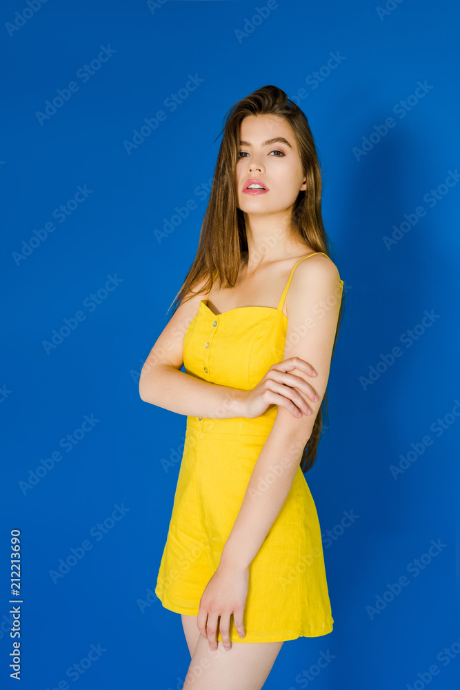 Elegant brunette woman in yellow dress posing on blue background Elegant brunette woman in yellow dress posing on blue background
