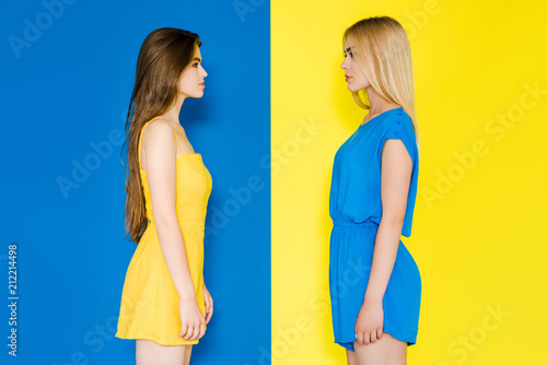 Female fashion models looking at each other isolated on blue and yellow background