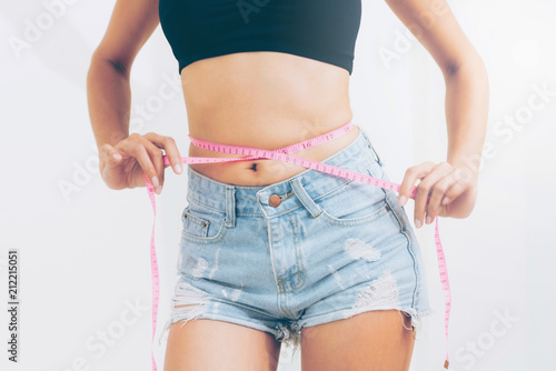 Obraz na plátne Slim woman measures her waist with measuring tape.