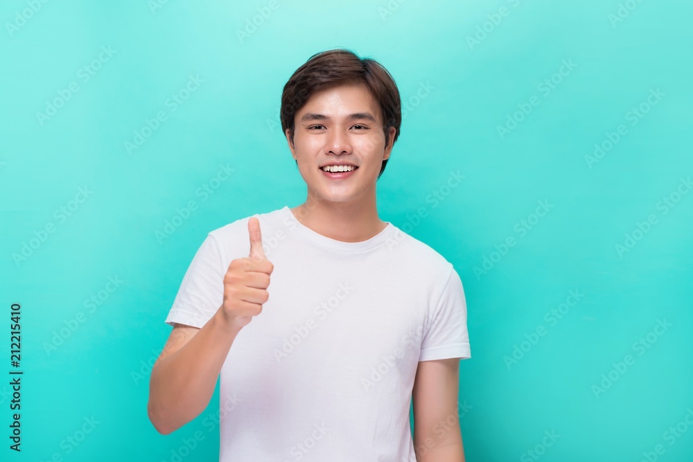 Young optimistic man isolated on blue background showing thump up with positive emotions of content and happiness. Concept of satisfaction with quality and recommendation Young optimistic man isolated on blue background showing thump up with positive emotions of content and happiness. Concept of satisfaction with quality and recommendation