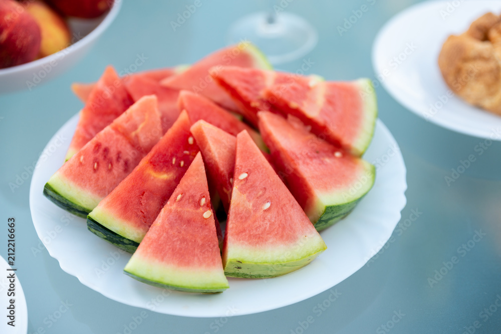View of tasty breakfast on glass table, juice fruits, nectarine, watermelon, pineapple, water and bake. Healthy, colorful and exotic food in paradise. Summertime concept. Palm leaf on background. View of tasty breakfast on glass table, juice fruits, nectarine, watermelon, pineapple, water and bake. Healthy, colorful and exotic food in paradise. Summertime concept. Palm leaf on background.