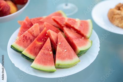 View of tasty breakfast on glass table, juice fruits, nectarine, watermelon, pineapple, water and bake. Healthy, colorful and exotic food in paradise. Summertime concept. Palm leaf on background.