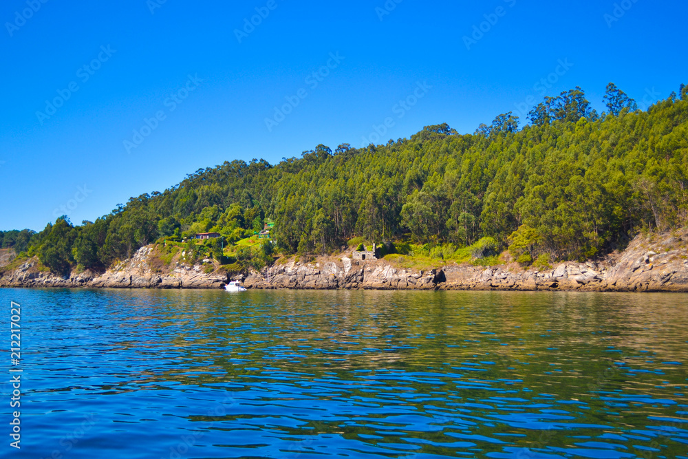 Cliff and forest in front of sea, with a boat diving. Cies islands, Galicia, Spain