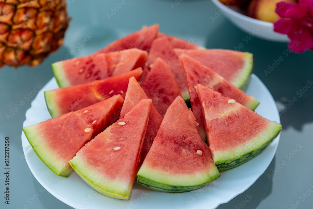 View of tasty breakfast on glass table, juice fruits, nectarine, watermelon, pineapple, water and bake. Healthy, colorful and exotic food in paradise. Summertime concept. Palm leaf on background.