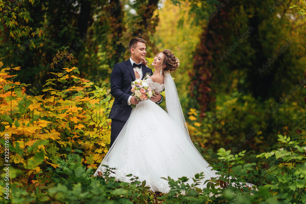 The groom tenderly embraces the bride's waist. Autumn multi colored forest. Nature