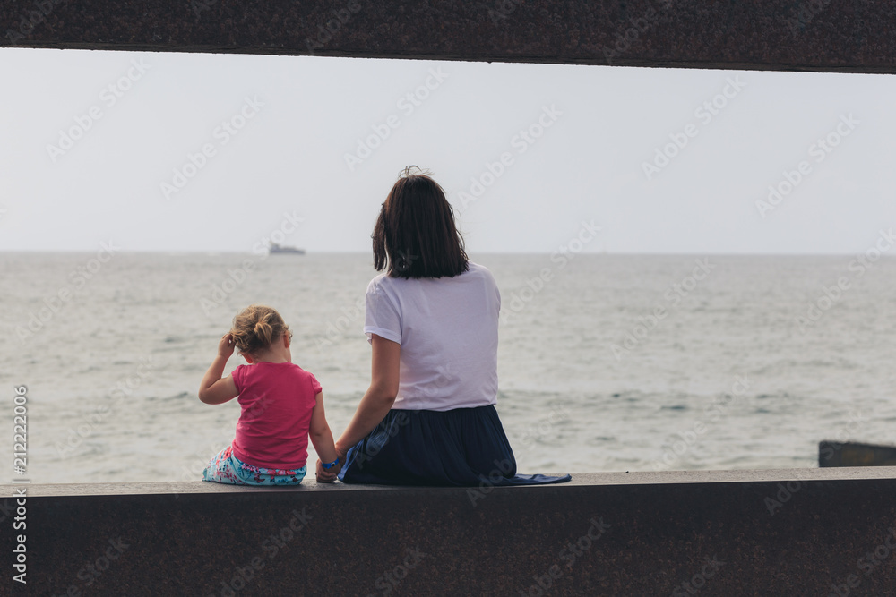 Mother with little daughter looks at the sea. Back view.