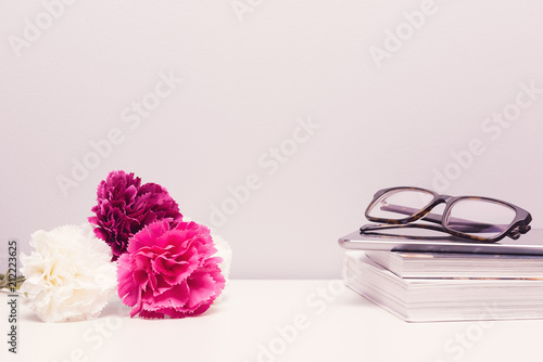 Feminine desktop bedside table with book, glasses, flowers and negative space, warm color background.