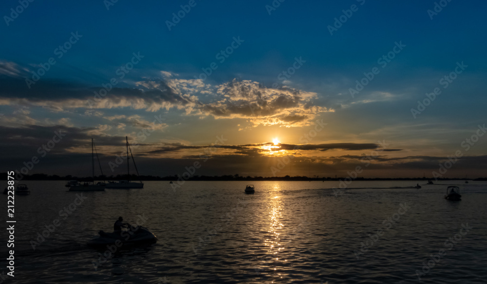 Power boats, sailboats and jet skis on the Guaiba river having a pleasure time during a wonderful sunset with blue and orange colors between some clouds in the sky