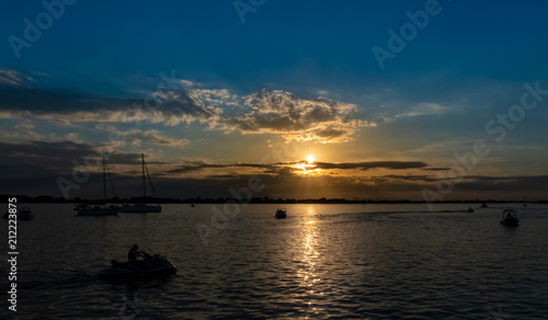 Power boats, sailboats and jet skis on the Guaiba river having a pleasure time during a wonderful sunset with blue and orange colors between some clouds in the sky © JArmando_ClauEleone