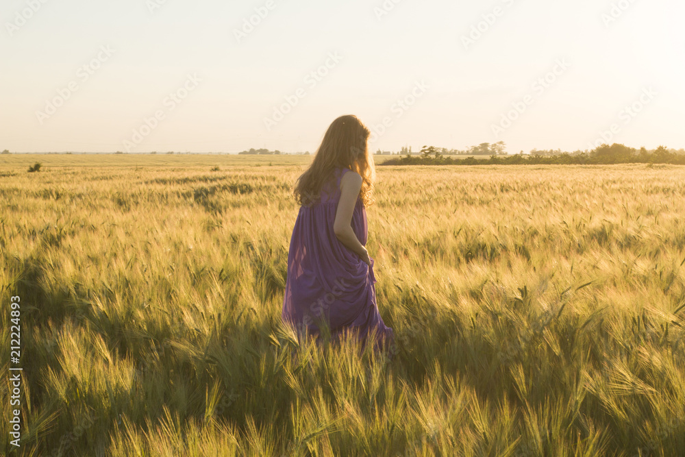 Young beautiful woman walking in summer wheat fields durinf sunset Young beautiful woman walking in summer wheat fields durinf sunset