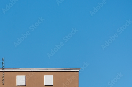 Close up in a partial geometric design of a top part of a modern building colored with a brown wall and details in white, along with a large space of a blue sky photo