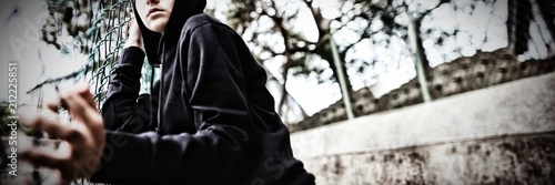 Anxious teenage girl leaning on wire mesh fence at school campus