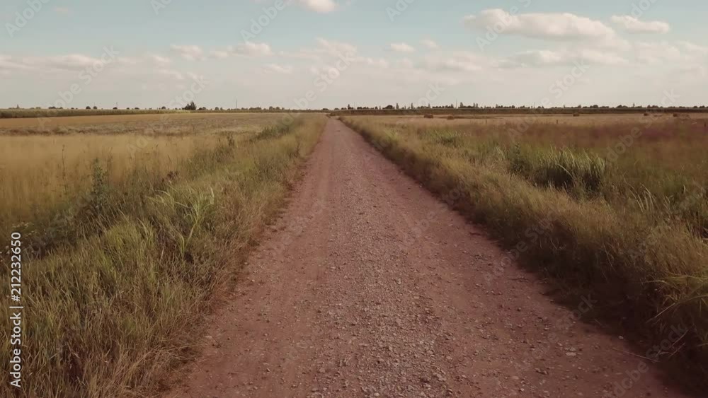 Empty country dirt road to infinity on sunny summer day, aerial view. Drone flying over land in low altitude flight and than raising high up to the sky. Empty country dirt road to infinity on sunny summer day, aerial view. Drone flying over land in low altitude flight and than raising high up to the sky.