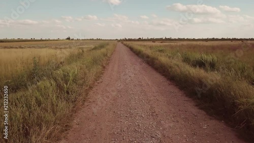 Empty country dirt road to infinity on sunny summer day, aerial view. Drone flying over land in low altitude flight and than raising high up to the sky.