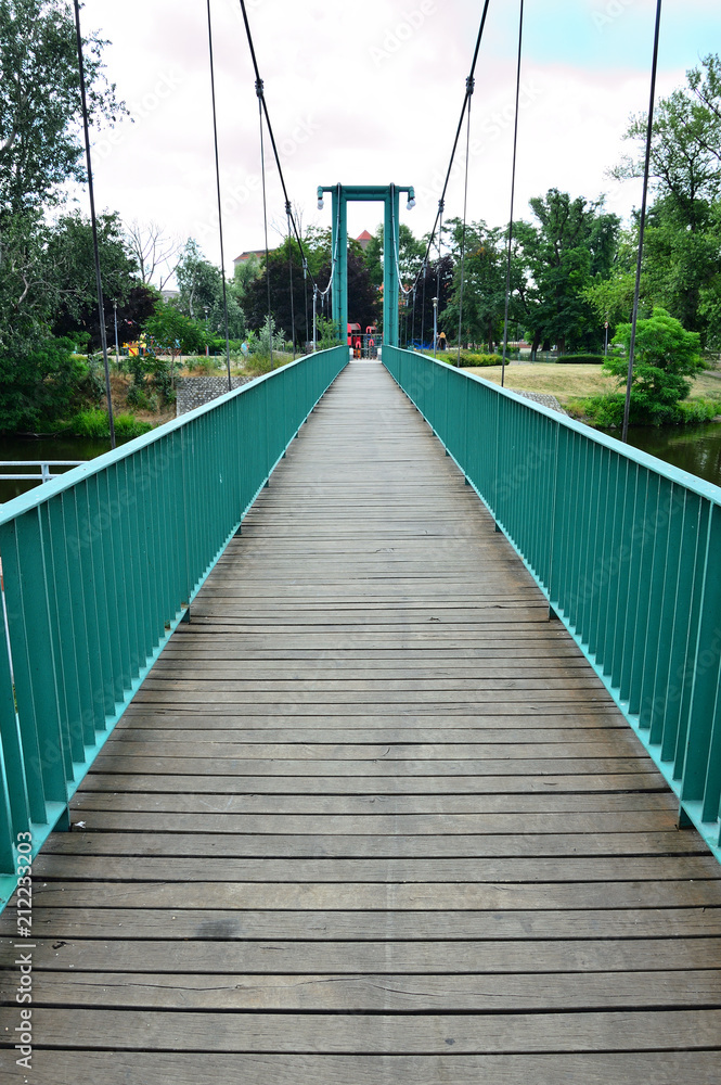 Stalowy most wiszący z drewnianym podestem.