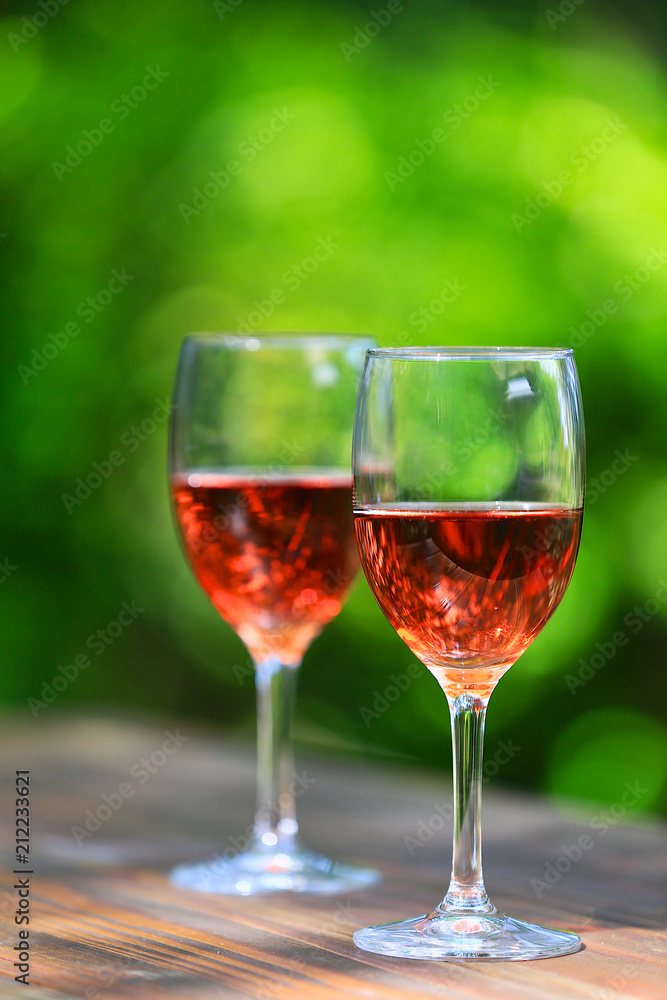 Two glasses of Shinning Rosé Wine on wooden table, defocused bright and fresh green outdoors background 1