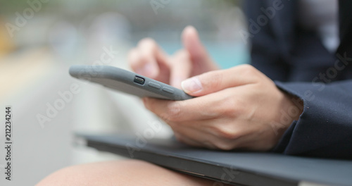 Businesswoman type on cellphone with her laptop computer at outdoor