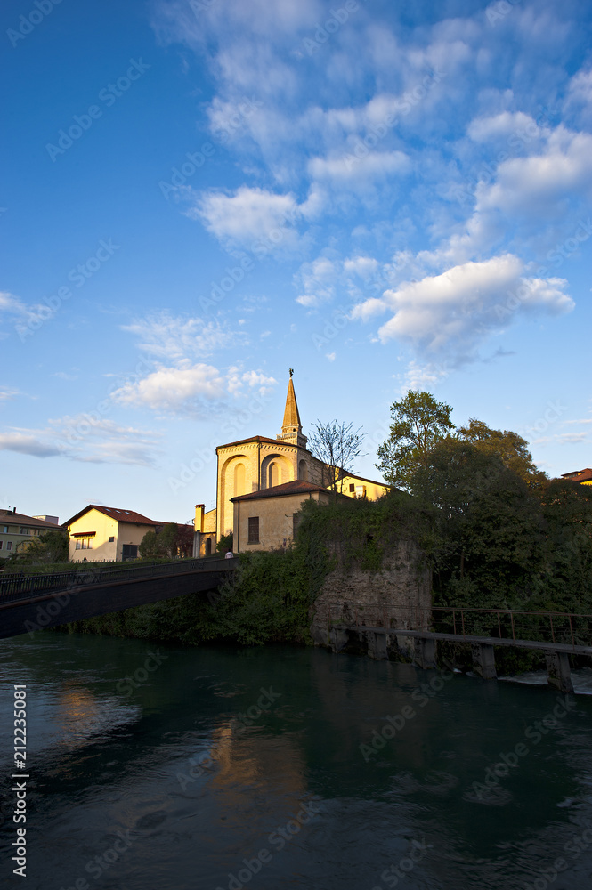 The bell tower of the cathedral of San Niccolò in Sacile is mirrored on the river livenza. Pordenone district. Italy