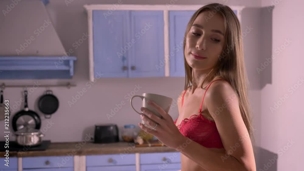 Young handsome woman in red bra holding cup of tea and standing in kitchen, perfect sexy body, attractive and seductive Young handsome woman in red bra holding cup of tea and standing in kitchen, perfect sexy body, attractive and seductive