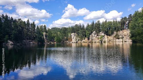 adrspach. the sky is reflected in the water of the lake with rocks and trees on the shore