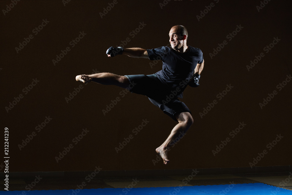 An adult athlete in black gloves beats a kick in a jump