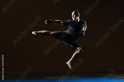 An adult athlete in black gloves beats a kick in a jump © andreyfire