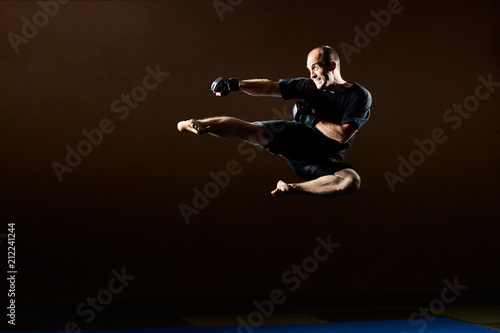 In a black T-shirt, an adult athlete beats a kick in a jump © andreyfire
