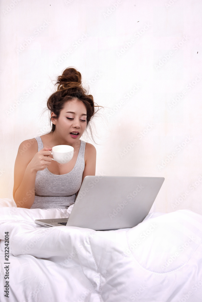 The lady iis using laptop and hold coffee cup in hand,very sleepy,in bedroom The lady iis using laptop and hold coffee cup in hand,very sleepy,in bedroom