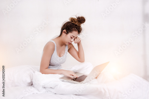 The lady is using laptop for work,very sleepy,in bedroom,blurry light around.