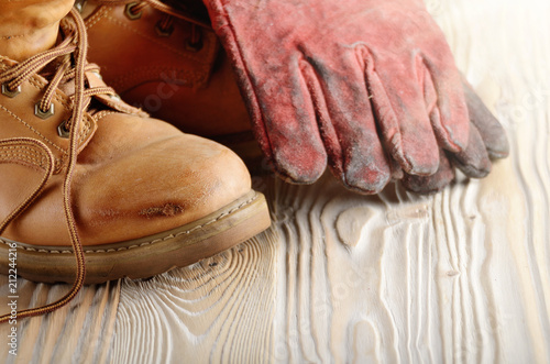 Yellow leather used work boots and protective gloves on wooden background closeup. Place for text