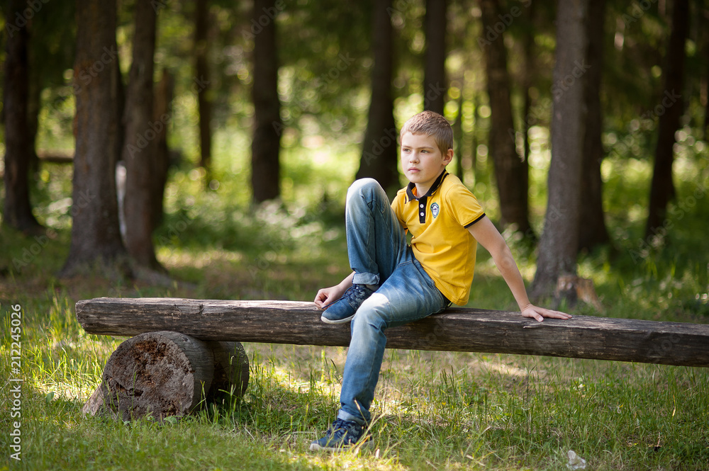 Fototapeta premium The boy is sitting on a bench in the forest.