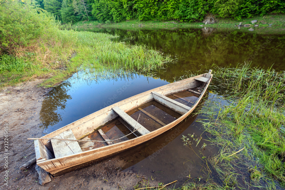 old wooden boat shore of river surrounded by forest at sunny summer day