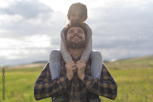 Padre juega con pequeña hija en día primaveral llevándola a hombros