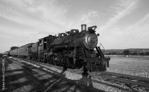 Steam train coming down tracks in a field in black and white