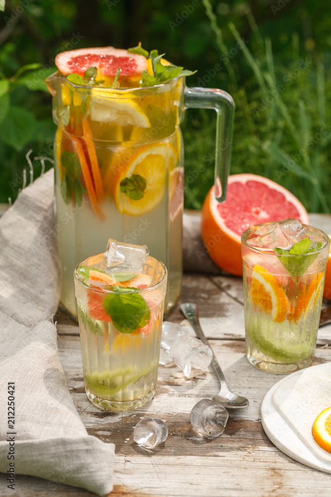 citrus lemonade in glass jug with mint. Orange. Grapefruit and lemon. On greenery background.
