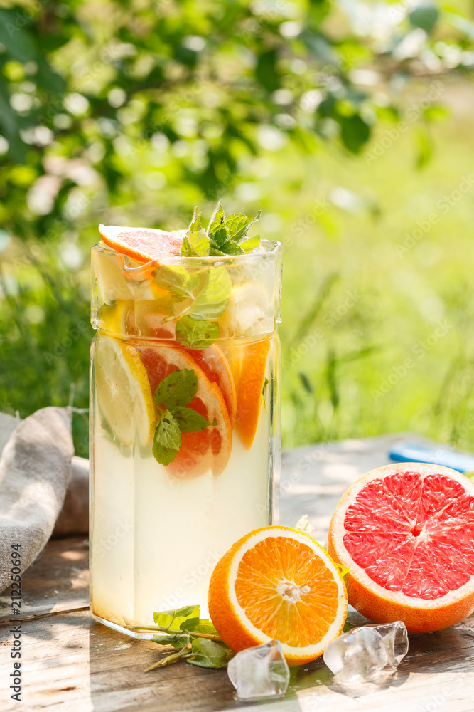 Fototapeta premium citrus lemonade in glass jug with mint. Orange. Grapefruit and lemon. On greenery background.