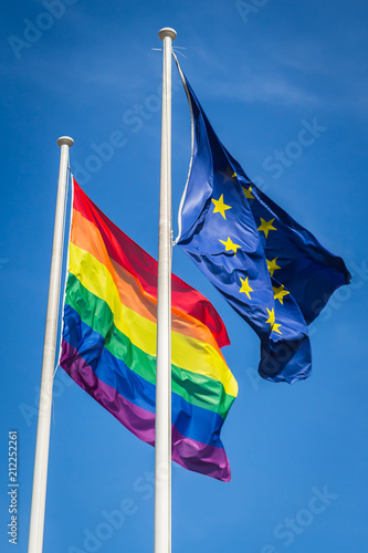 Rainbow flag and EU flag waving in the wind, sunny day, blue sky