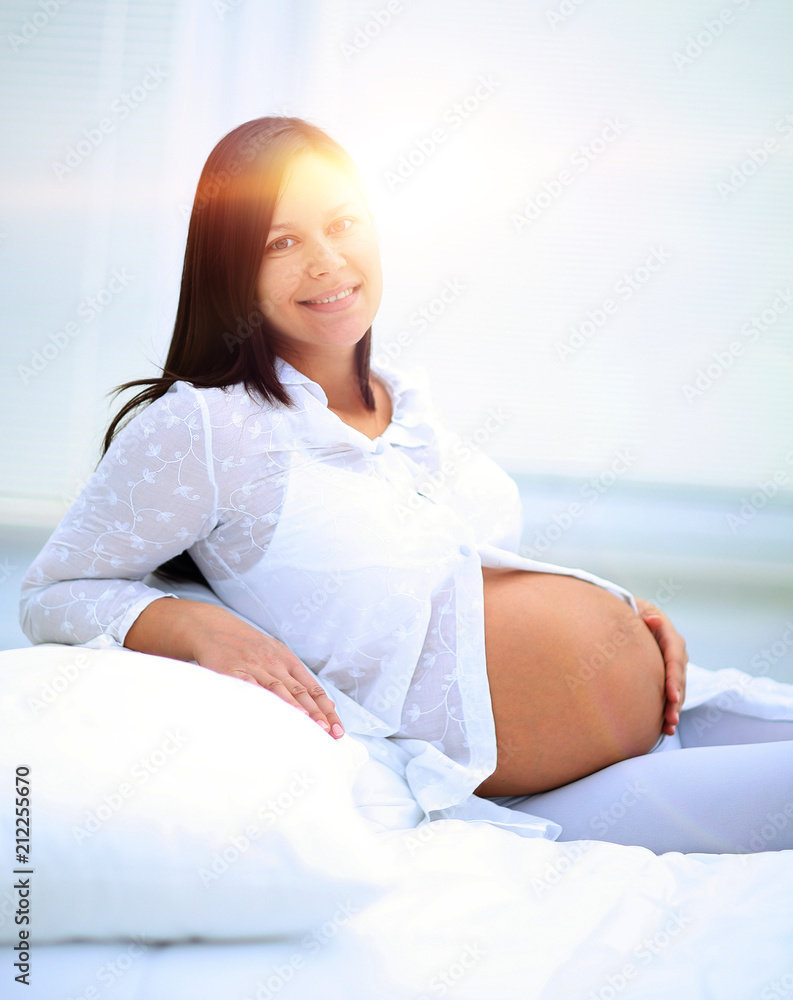 Beautiful pregnant woman sitting at sofa and keeping hand on belly. Beautiful pregnant woman sitting at sofa and keeping hand on belly.