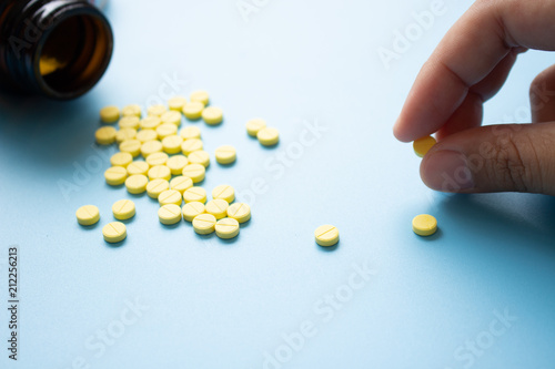 Foto Hand pick up yellow pill with bottle and medicine on light blue background