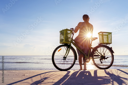 Woman spending day off on a beach, bicycle and girl silhouette in sunlight