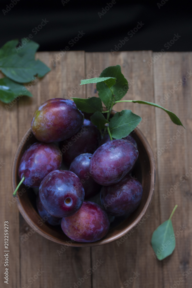 full rural bowl of large ripe blue plums on a wooden table vertically