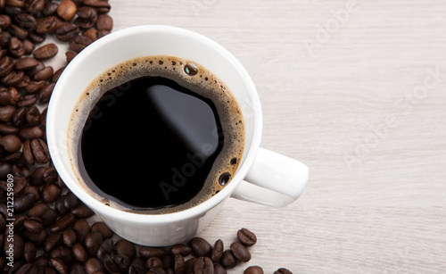 white cup of coffee with foam against a background of fried coffee beans