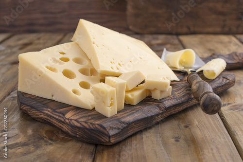 Cheese with holes large and small. Wooden board and knife. Traditional Dutch cheese. Copy space photo