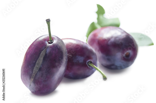 three ripe whole big blue plums in a row