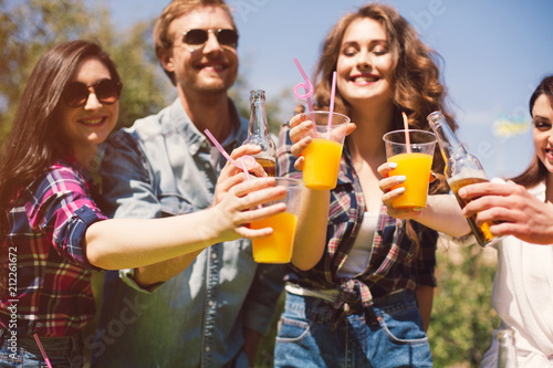 Cheerful group of friends toasting their drinks. Happy young people spending time outdoors on sunny day cheering their orange juices.
