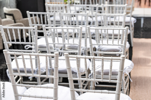 White wedding chairs closeup for ceremony with background of rows of many seats pattern, aisle and podium in venue, restaurant, building outdoors © Kristina Blokhin