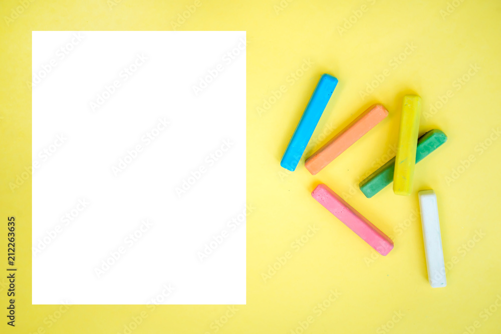 Colorful crayons and a sheet of white paper on a yellow background Colorful crayons and a sheet of white paper on a yellow background