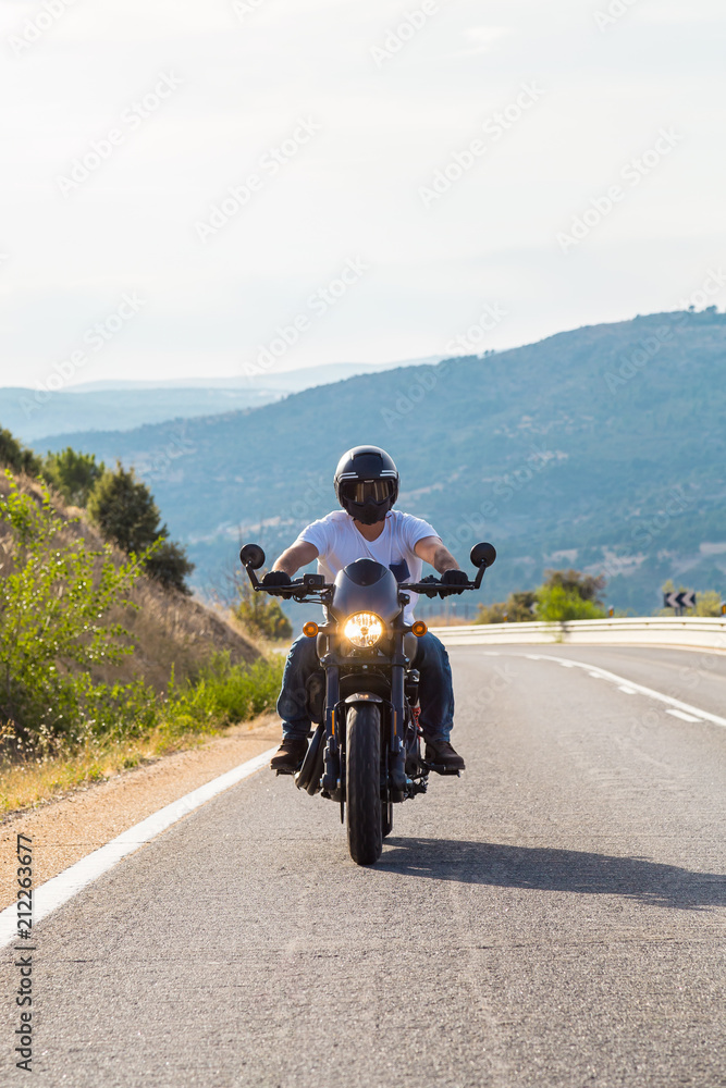 Naklejka premium Young man riding a motorcycle on road in mountains in sunny day. 