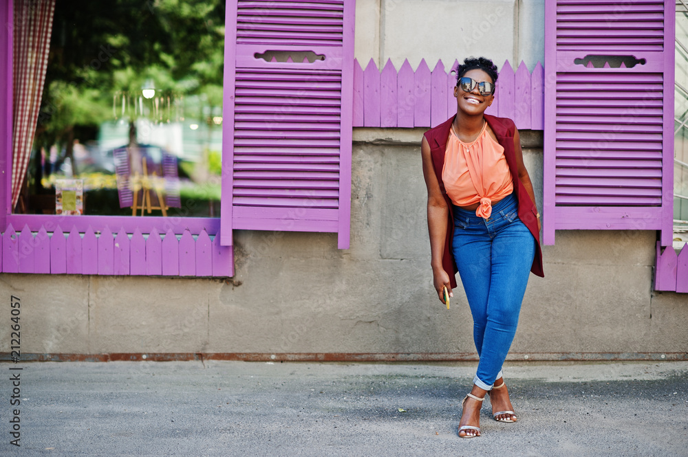 African american girl in sunglasses posed against purple windows with cell phone at hand.